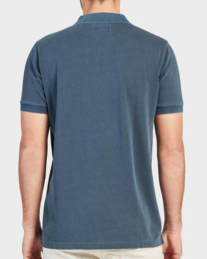 Rear view of a person wearing a blue Academy Brand Academy Polo, made from comfortable Cotton Pique fabric, paired with beige pants. The background is plain and light-colored.