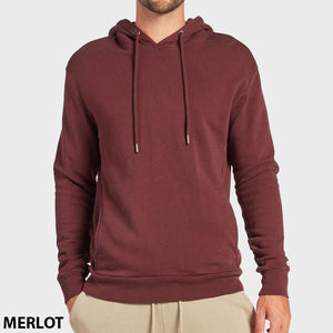 A person wears a comfy merlot Academy Brand Boston Hoodie with drawstrings and beige pants, standing against a white background. "MERLOT" is displayed in bold black text at the lower left corner.