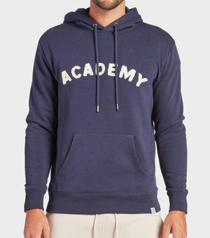 A person wears the Academy Brand College Hoodie in navy, featuring “ACADEMY” in textured white letters across the chest, a front pocket, and drawstrings. The person's head is out of frame.