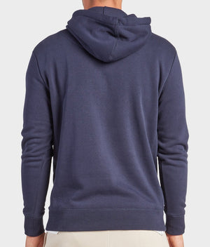 A person is seen from behind wearing the Academy Brand College Hoodie in dark blue. The plain, long-sleeve sweatshirt pairs with light pants, creating a casual look against a plain, light background.