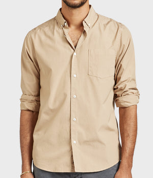 Someone is wearing the Academy Brand Frank Poplin Shirt in beige, made of 100% cotton for comfort, featuring rolled-up sleeves and a chest pocket. It is paired with dark pants against a light grey background.