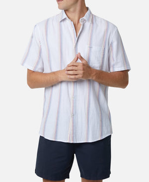 A person wearing the Industrie The Zante S/S Shirt, a casual, short-sleeve, button-up shirt made from 100% cotton with vertical stripes in blue, red, and gray tones, paired with dark blue shorts. The individual is standing with hands clasped together, slightly angled to the right against a plain white background.