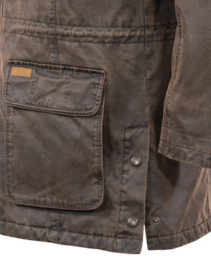 Close-up of a weathered brown Outback Nolan Jacket showing a large front pocket with a flap and a small label on the top left corner. The jacket features visible stitching and two metal snap buttons below the pocket. The rugged texture appears durable, making it an ideal water-resistant jacket.