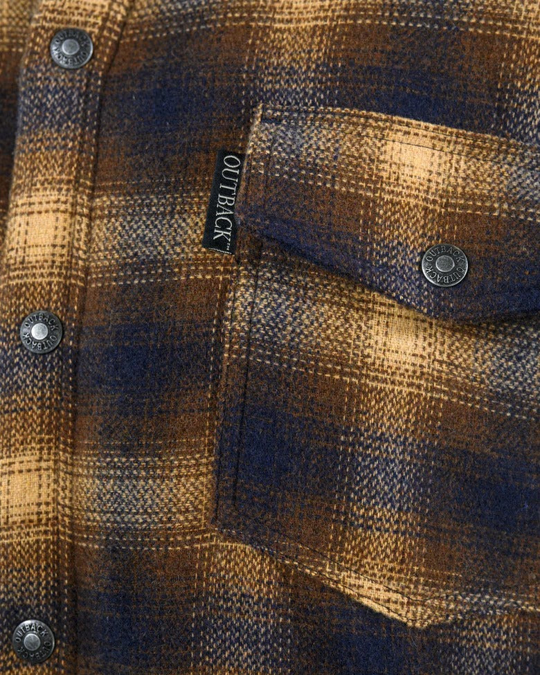 Close-up of the Outback Arden Jacket shows a plaid pocket in brown and blue tones. The jacket, with snap buttons and an "OUTBACK" label above the pocket, features a soft berber fleece lining for comfort and warmth.