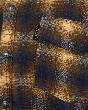 Close-up of the Outback Arden Jacket shows a plaid pocket in brown and blue tones. The jacket, with snap buttons and an "OUTBACK" label above the pocket, features a soft berber fleece lining for comfort and warmth.