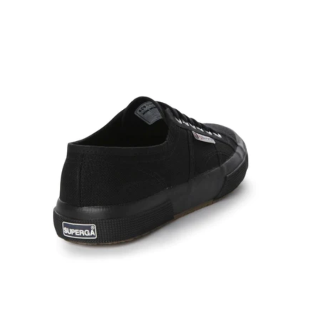 A single Superga Cotu Classic Sneaker in black with a low-cut design features a canvas upper, black laces, and rubber sole. The "Superga" logo is on the heel plate. It is shown at a slight angle, revealing the back and side views.