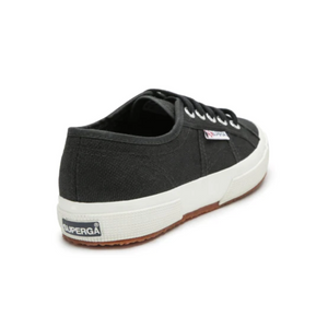 The Superga Cotu Classic Sneaker is black with white laces and a thick sole, featuring the iconic "Superga" logo tag on the heel. Its premium canvas upper has stitching details, and it sports a brown gum sole, embodying Superga's craftsmanship.