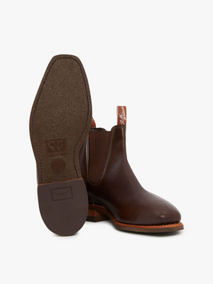The RM Williams Comfort Kangaroo Craftsman Boots are displayed, with one boot standing upright and the other positioned to showcase the sole, emphasizing the intricate stitching details and branding. Handcrafted in Australia, these brown leather cowboy boots feature pull tabs, a classic design with a smooth finish, and a comfort innersole.