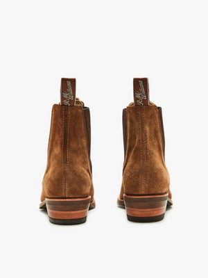 Rear view of RM Williams Lady Yearling suede rubber sole boots, showcasing brown suede Chelsea style with wooden block heels and elegant elastic sides. They feature pull tabs with silver writing, all set against a plain white background.