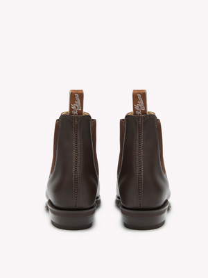 Rear view of RM Williams Adelaide Rubber Sole Boots in sleek brown leather with pull tabs displaying brand text. The polished leather boots rest on dark soles, exuding a smart-casual appeal against a plain, light background.