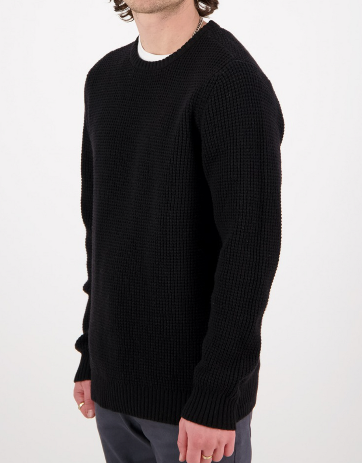 A person wears the Swanndri Fistral Waffle Knit in black over a white shirt and dark pants, standing against a plain white background with their head partially out of the frame.
