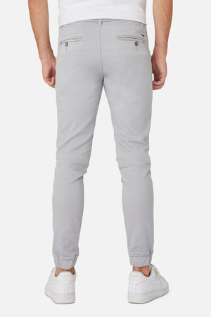 Someone is seen from the back wearing Industrie The Drifter Chino Pant in light gray, featuring a slim-fit jogger style with an elastic waist and buttoned back pockets, paired with white sneakers, set against a plain white background.