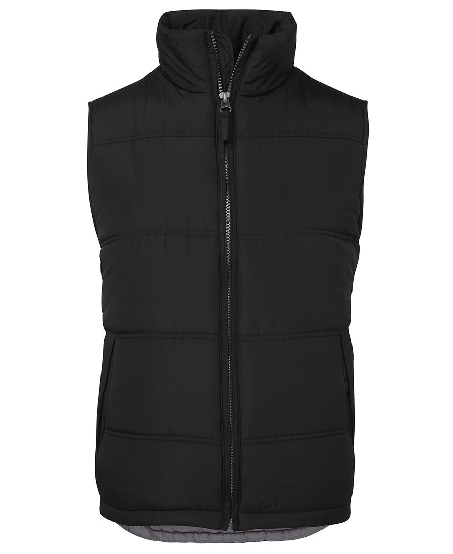 The JBs Adventure Vest is a sleeveless black puffer with extra thick fill, front zipper, high collar, and two side pockets—displayed on white background—making it a cozy, casual choice for urban style.