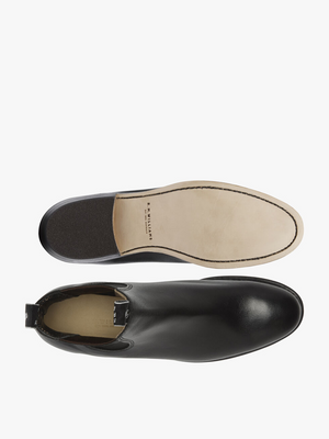 Top-down view of a pair of RM Williams Adelaide Kangaroo Boots in black; one highlights the smooth leather upper, while the other reveals a light tan sole with stitching and branding—ideal for smart-casual style.