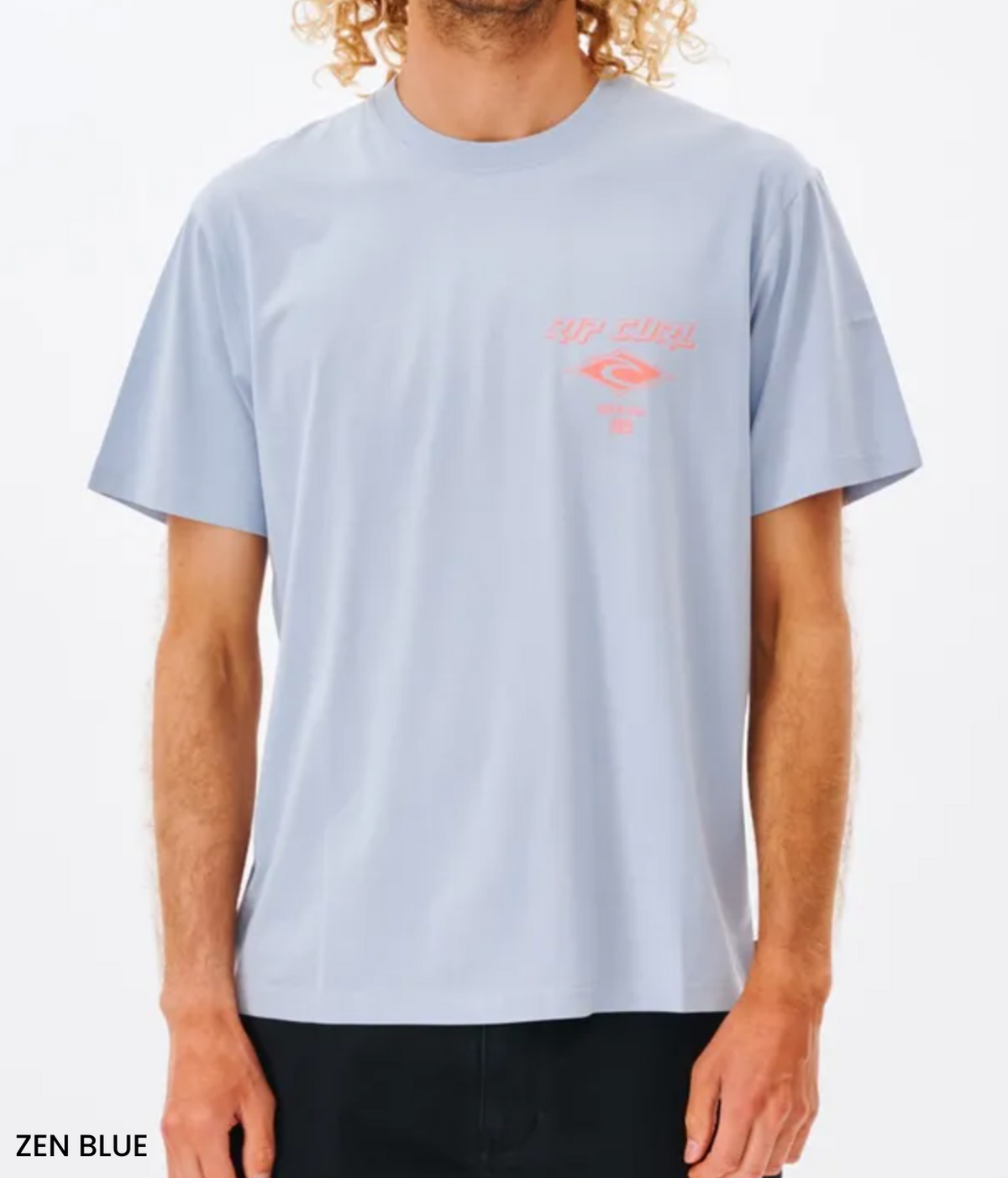 The person is wearing the Rip Curl Fade Out Icon Tee in light blue with a pink graphic and text on the left chest. Made from organic cotton, it has a relaxed fit, pairing well with dark pants against a plain white background. "Zen Blue" is elegantly written in the bottom left corner.