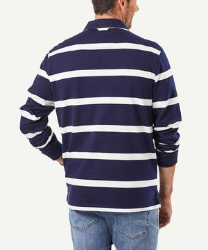 A man is standing with his back to the camera, wearing a stylish Gazman Classic Stripe Rugby, which features long sleeves and dark blue and white horizontal stripes. He is also wearing light blue jeans. The background is plain white.