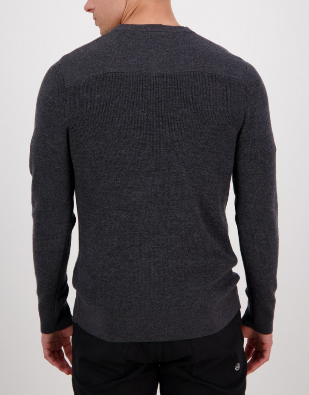 A man is shown from behind wearing the Swanndri Otahu River Crew Neck Merino Knit in dark gray with black pants, standing against a plain light background. For the best fit, refer to our size guide or check the half chest measurement.