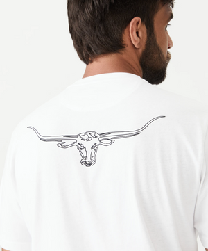 A man with short dark hair and a beard is turned away from the camera, wearing an RM Williams Longhorn Byron Tee made of premium cotton jersey. The back of this unisex style shirt features a simple black line drawing of a longhorn steer skull with extended horns. The background is plain and white.