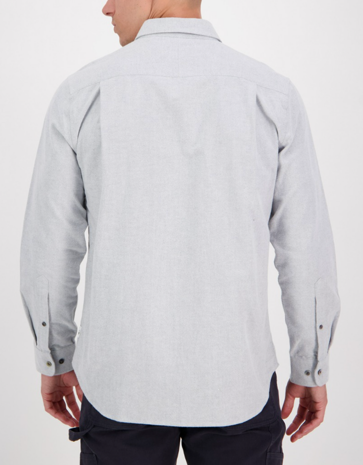 The individual, viewed from behind, wears the stylish Swanndri Marwood Shirt in light gray. It's a long-sleeved, button-up shirt with a classic collar and buttoned cuffs, crafted from 100% cotton. It pairs well with their dark pants against the plain white background.