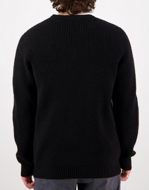A person with curly brown hair is shown from behind, wearing the Swanndri Fistral Waffle Knit in black and gray pants against a plain white background.