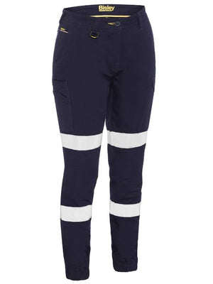 The Bisley Women's Taped Cuffed Cargo Pant in dark blue features durable cotton fabric, white reflective tape above and below the knees, side pockets, and a yellow zipper for high visibility and safety.
