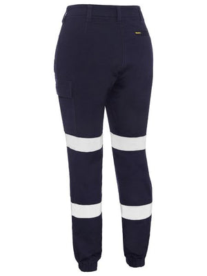 The Bisley Womens Taped Cuffed Cargo Pant, in navy blue cotton, includes two white reflective bands per leg for visibility, a side cargo pocket for practicality, and elastic ankle bands for a snug fit.