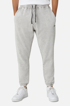 A person wears Industrie The Del Sur Track Pant in light gray, featuring a relaxed fit, elastic drawstring waist, side pockets, elastic ankle cuffs, and a subtle embroidered Industrie logo. White sneakers are worn; upper body is not shown.
