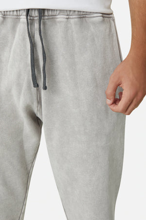Close-up of a person wearing Industrie The Del Sur Track Pant in light gray, featuring a black elastic drawstring waist. They wear a white shirt, with their right hand barely visible. The image highlights the joggers' texture and fit along with the subtle Industrie logo.