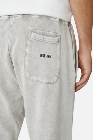 Someone is casually dressed in Industrie The Del Sur Track Pant, featuring light gray joggers with an elastic drawstring waist and a visible back pocket showcasing the distinctive Industrie logo, paired effortlessly with a partially visible white shirt for a laid-back look.