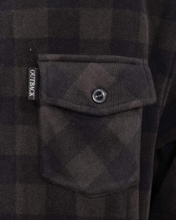Close-up of a black and dark brown plaid fabric with a buttoned pocket, designed in mid-weight shirt style. The pocket seam has a fabric tag reading "OUTBACK" in white, adding style to the 100% polyester Outback Men's Big Shirt.