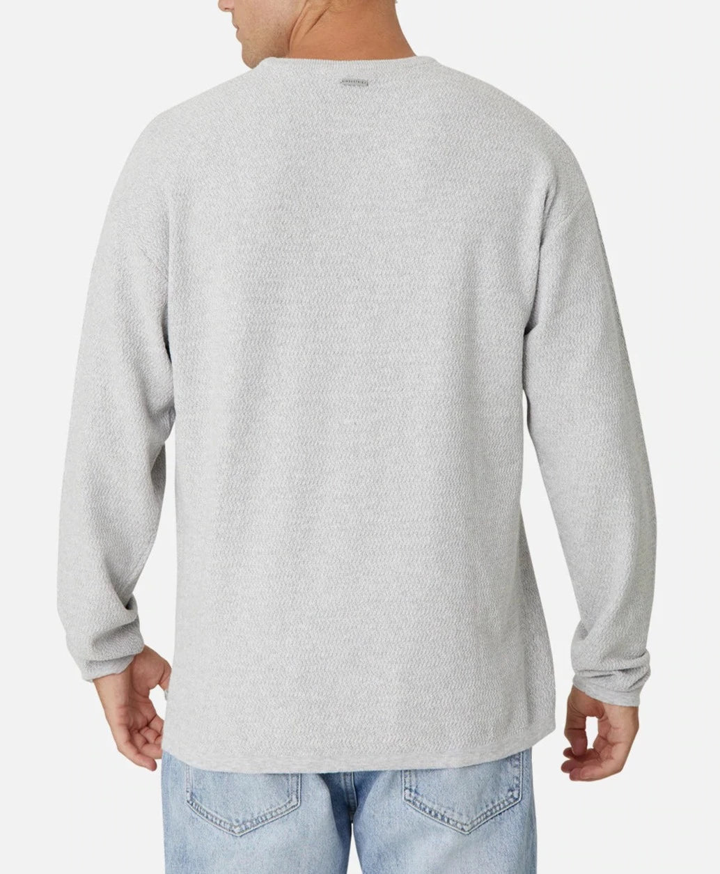 A person is shown from behind wearing an oversized fit, long-sleeve, light gray Industrie The Aries Knit and light blue jeans. The 100% cotton shirt has a subtle texture and a small brand logo at the upper center back. The background is plain white.