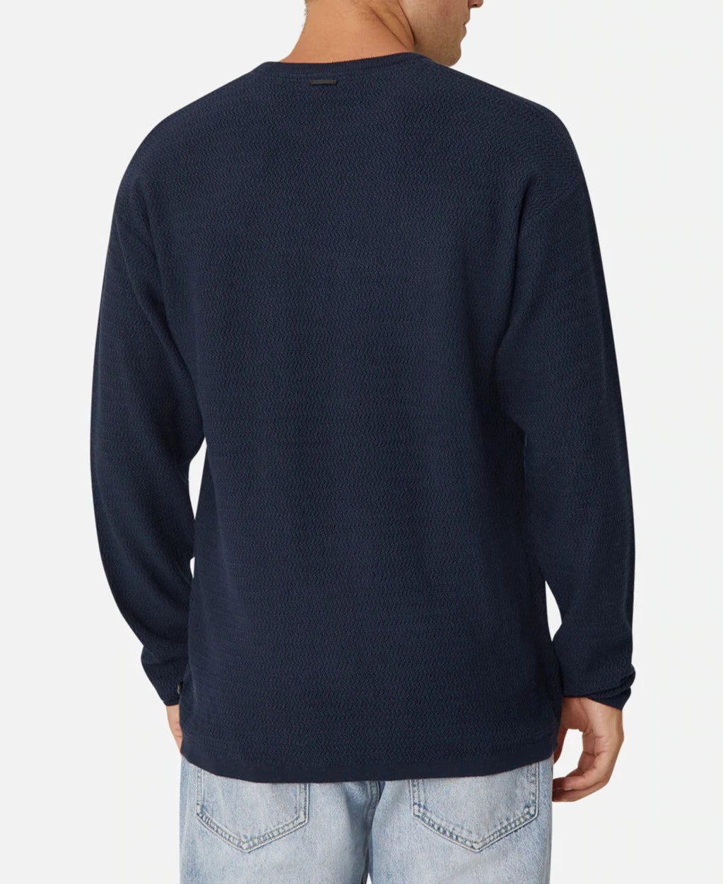 A person is wearing the Industrie The Aries Knit, an oversized navy blue long-sleeve shirt made from 100% cotton with a textured pattern, and light blue jeans. They're viewed from the back against a plain white background.