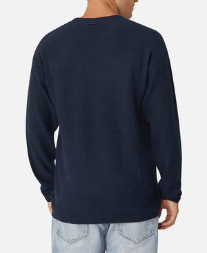 A person is wearing the Industrie The Aries Knit, an oversized navy blue long-sleeve shirt made from 100% cotton with a textured pattern, and light blue jeans. They're viewed from the back against a plain white background.