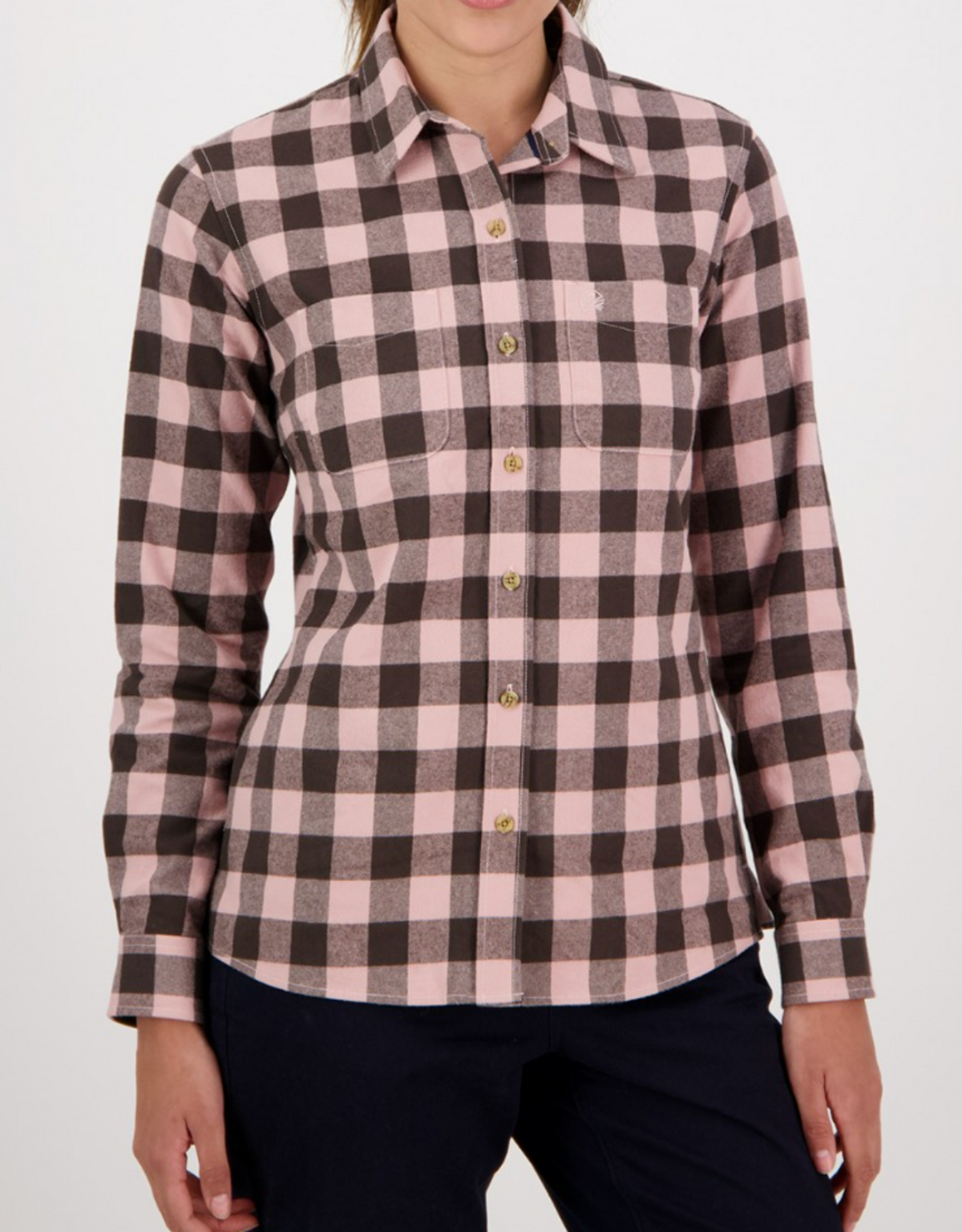 A person wearing a Swanndri Women's Taranaki Tailor Shirt in pink and black checkered pattern paired with dark pants. The 100% cotton shirt has buttons and a front left pocket, but the individual's head is not visible in the image.