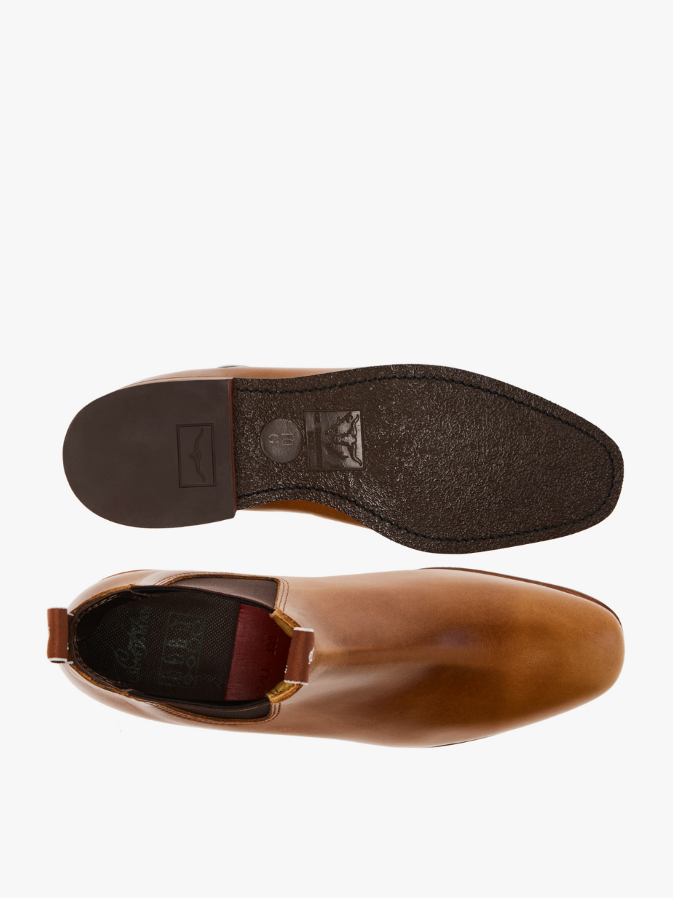 The RM Williams Comfort Craftsman Boot in tan pull-up leather is shown from above, highlighting the top view of one boot and the textured black sole and heel of the other, handmade in Adelaide against a white background.