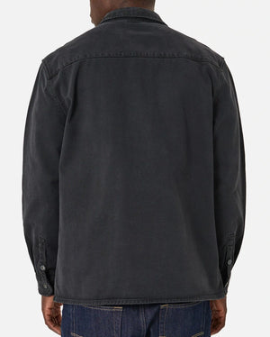 A person in the Industrie The Woodbury Shirt, a comfortable dark cotton button-up with long sleeves, and denim jeans, stands against a plain light background.