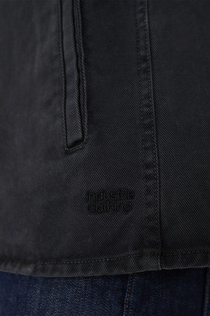 Close-up of a black cotton Industrie The Woodbury Shirt with a vertical pocket and stitching detail. "Industrié Clothing" is subtly displayed on the fabric. Comfortable and stylish, it pairs effortlessly with dark blue denim jeans for a chic look.