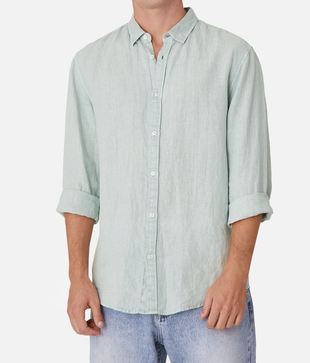 A person wears the Industrie The Tennyson Linen Shirt, a light blue-green 100% linen button-up with rolled sleeves and a subtle marle texture, paired effortlessly with light blue jeans against a plain white backdrop.