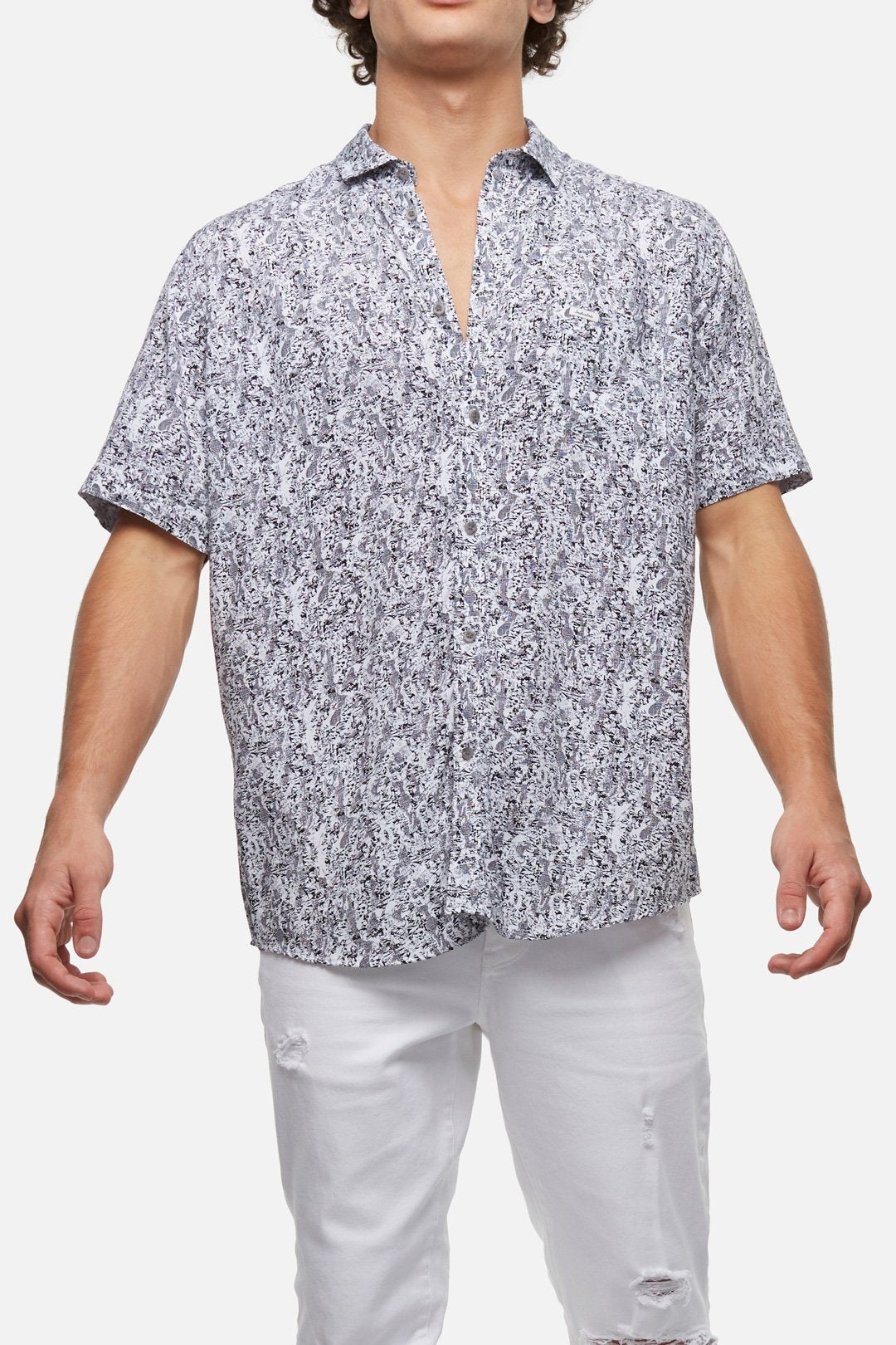 The individual is wearing the Industrie The Santa Cruz Shirt, which features short sleeves and a button-up design with a stylish black and white abstract pattern. Made from 100% Viscose, this comfortable shirt is paired with white distressed jeans. Standing with arms slightly out to the sides, they display the outfit against a plain white background.