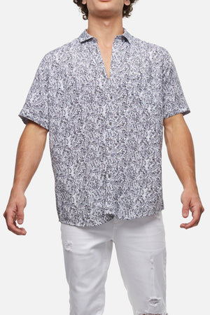 The individual is wearing the Industrie The Santa Cruz Shirt, which features short sleeves and a button-up design with a stylish black and white abstract pattern. Made from 100% Viscose, this comfortable shirt is paired with white distressed jeans. Standing with arms slightly out to the sides, they display the outfit against a plain white background.