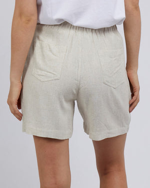 A person is seen from behind wearing Foxwood Ellie Shorts in beige linen blend with a white top. The relaxed-fit shorts have an elastic waistband and two back pockets, set against a plain gray background.