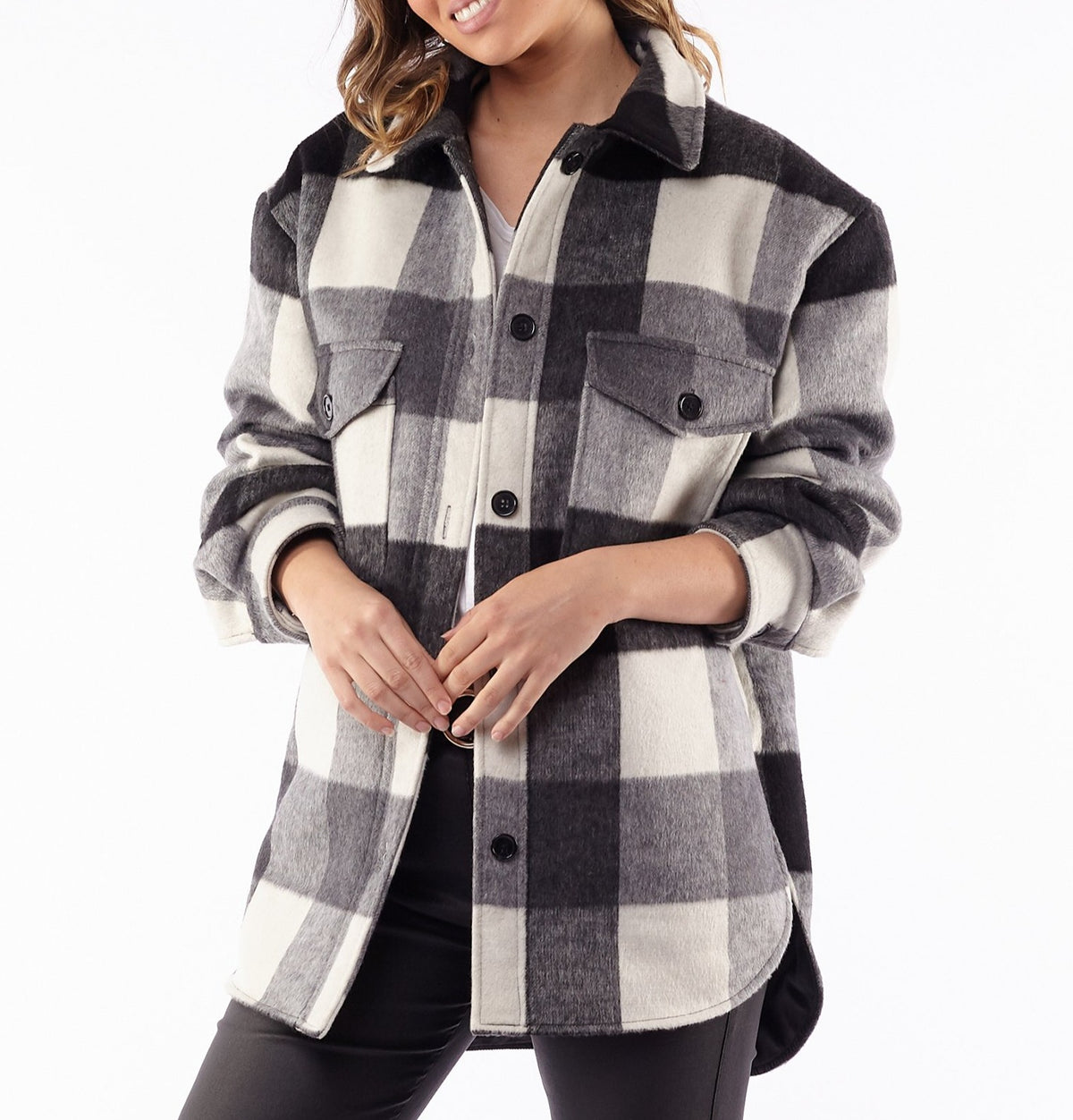 Woman wearing the Foxwood Lyon Shacket in black, white, and gray plaid with front pockets and polyester lining, standing against a white background. She tilts her head slightly and clasps her hands in front.