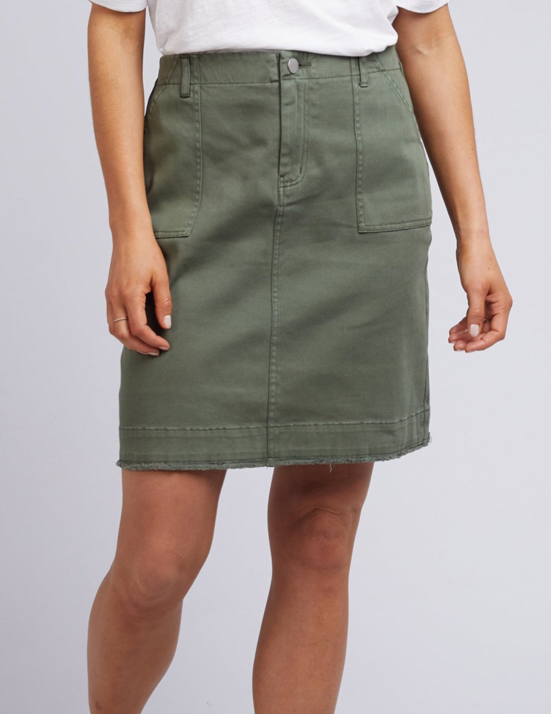 A person is wearing a white top with an olive green Foxwood Charlee Skirt featuring front pockets, visible buttons, and stitching details on a plain, light background.