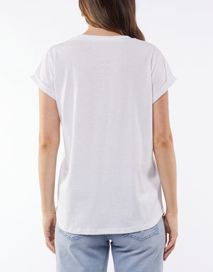 A person with long hair, back to the camera, wears a Foxwood Signature Tee known for its lightweight, breathable material. It's casually paired with light blue jeans against a plain white background, highlighting this wardrobe staple effortlessly.