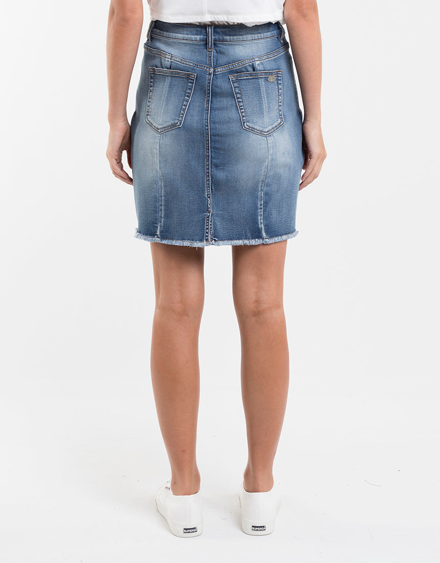 Rear view of a person in a Foxwood Kiama Skirt featuring a frayed hem and two pockets, paired with white sneakers, set against a plain white background for a casual style vibe.