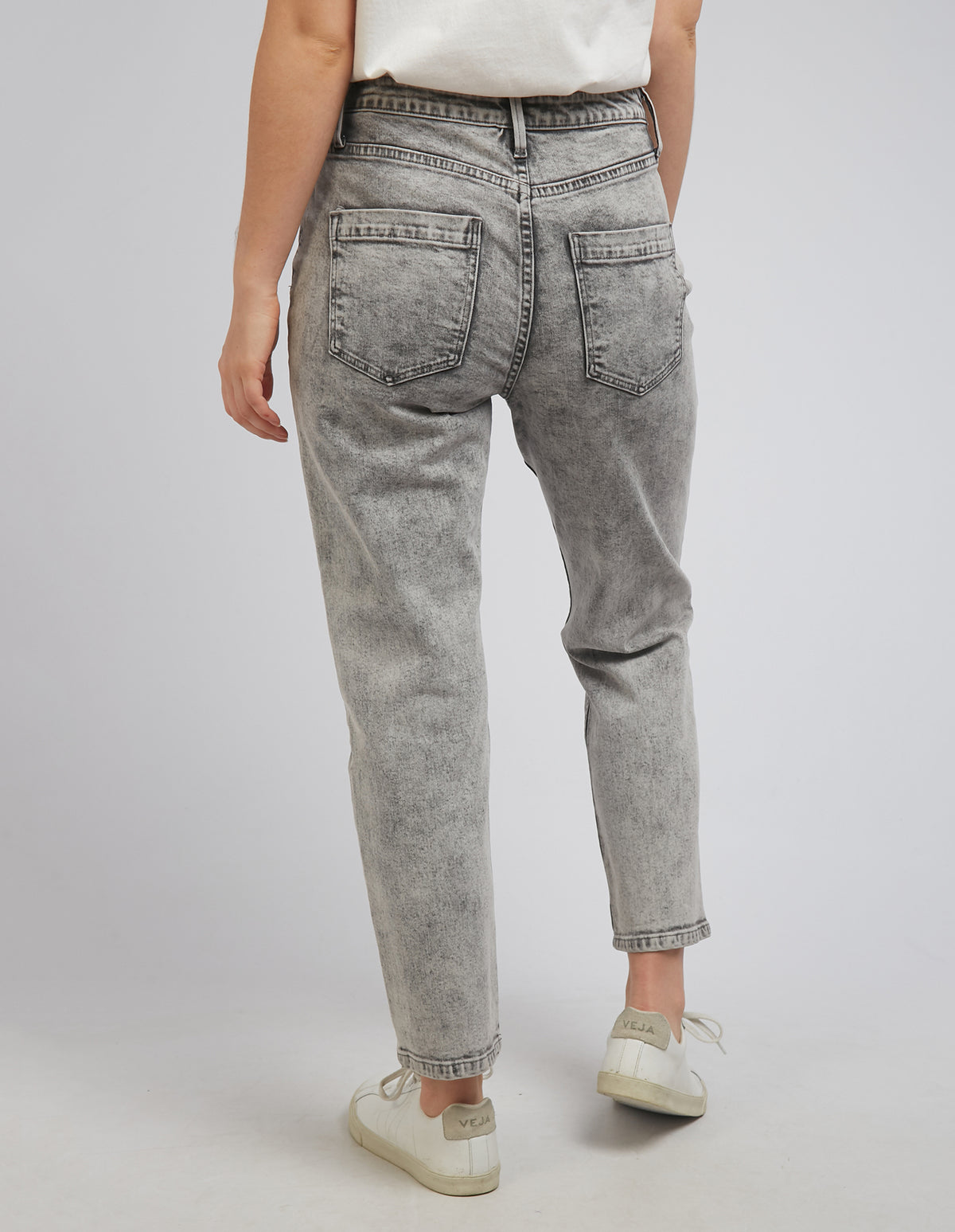 A person is seen from behind wearing Foxwood Barkly Straight Leg Jeans, offering a comfortable stretch fit, and paired with a white shirt. The outfit is completed with white sneakers against a plain, light gray background.