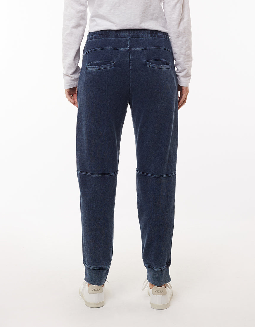 A person wearing a white long-sleeve shirt and the Foxwood Annie Pant, noted for their comfortable style and subtle denim wash, is shown from the back. They are also wearing white sneakers with "VEJA" written on the heel. The Foxwood Annie Pants have back pockets and visible seam details above the knees. The background is plain white.