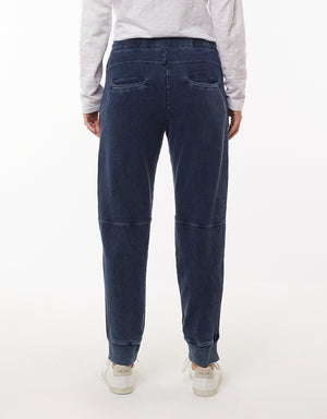 A person wearing a white long-sleeve shirt and the Foxwood Annie Pant, noted for their comfortable style and subtle denim wash, is shown from the back. They are also wearing white sneakers with "VEJA" written on the heel. The Foxwood Annie Pants have back pockets and visible seam details above the knees. The background is plain white.