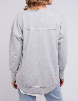 A person wears a gray cotton jumper with seam details and light blue jeans. Facing away from the camera, they showcase the Foxwood Simplified Crew against a plain light gray background.