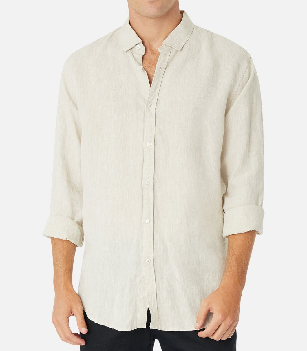 A person wears the Industrie The Tennyson Linen Shirt, a beige long-sleeve button-up with rolled-up sleeves, offering a relaxed fit made from 100% linen, paired with sleek black pants against a plain white background.